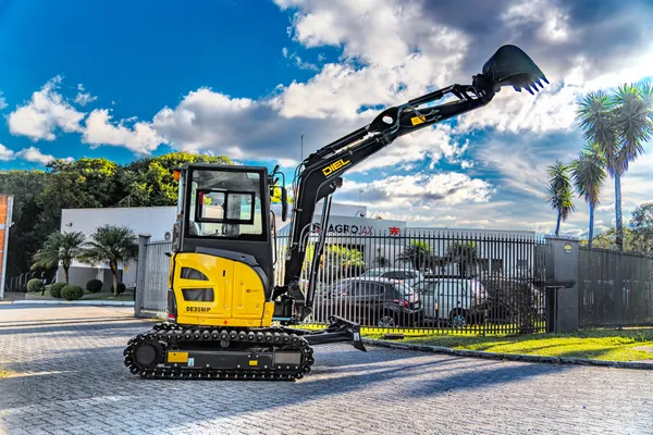 Mini escavadeira DIEL DE35MP com o braço elevado em frente à unidade Agrojax