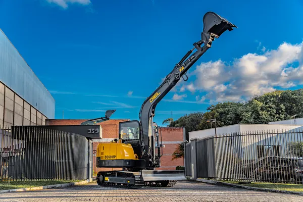 Escavadeira DIEL DE60MP com o braço elevado, em vista ampla junto ao portão da Agrojax
