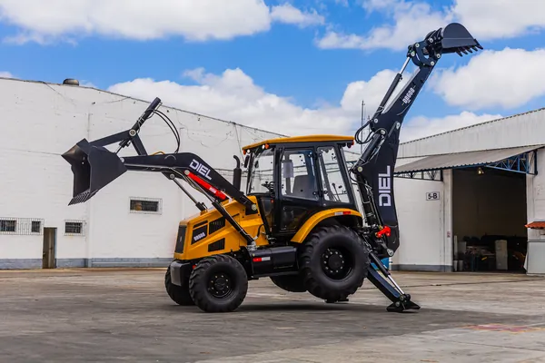 Retroescavadeira DIEL DR608 com o braço traseiro elevado e estabilizadores apoiados